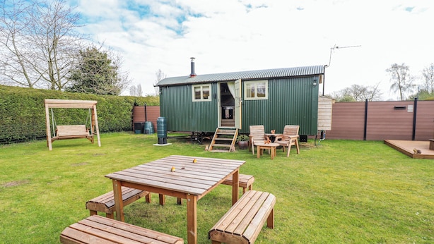 A green metal shed with a ladder, a swing, and wooden furniture in a grassy yard. - Twit Twoo Shepherds Hut (Louth)