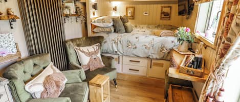A cozy room with a bed, a green armchair, a wooden side table, and a small wooden chest.