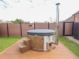 Un jacuzzi con una terraza de madera, una chimenea de metal y una valla de madera al fondo.