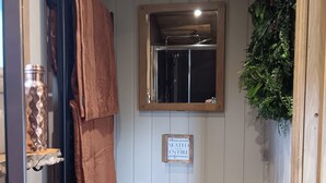 A bathroom with a towel rack, a sign instructing to remain seated, a mirror, and a toilet paper holder. - Twit Twoo Shepherds Hut (Louth)