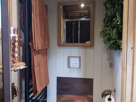 A bathroom with a towel rack, a sign instructing to remain seated, a mirror, and a toilet paper holder.