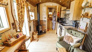 A cozy room with a fireplace, wooden furniture, and a kitchen area. - Twit Twoo Shepherds Hut (Louth)