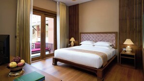 A hotel room with a bed, two bedside lamps, a television, a wooden floor, and a balcony with a view. - Royal Palace Hotel (Nyaung-U)