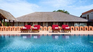 A pool with lounge chairs, a covered area with a tiled roof, and a brick wall. - Royal Palace Hotel (Nyaung-U)