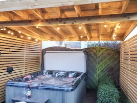 Un jacuzzi con terraza de madera, luces cálidas y valla de madera.