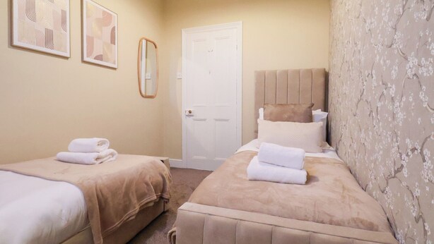 A hotel room with two beds, a door, and two framed artworks on the wall. - Crescent Bay House (Filey)
