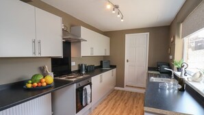 A modern kitchen with white cabinets, a black countertop, a built-in oven, and a window with a view. - Crescent Bay House (Filey)