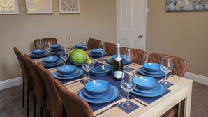 A dining room with a round table set for six, blue plates, and a bottle of Prosecco. - Crescent Bay House (Filey)