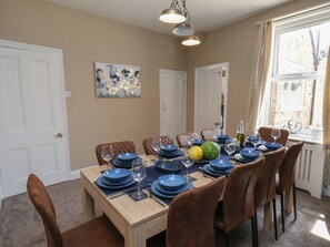 A dining room with a wooden table set for eight, brown upholstered chairs, and a painting on the wall.