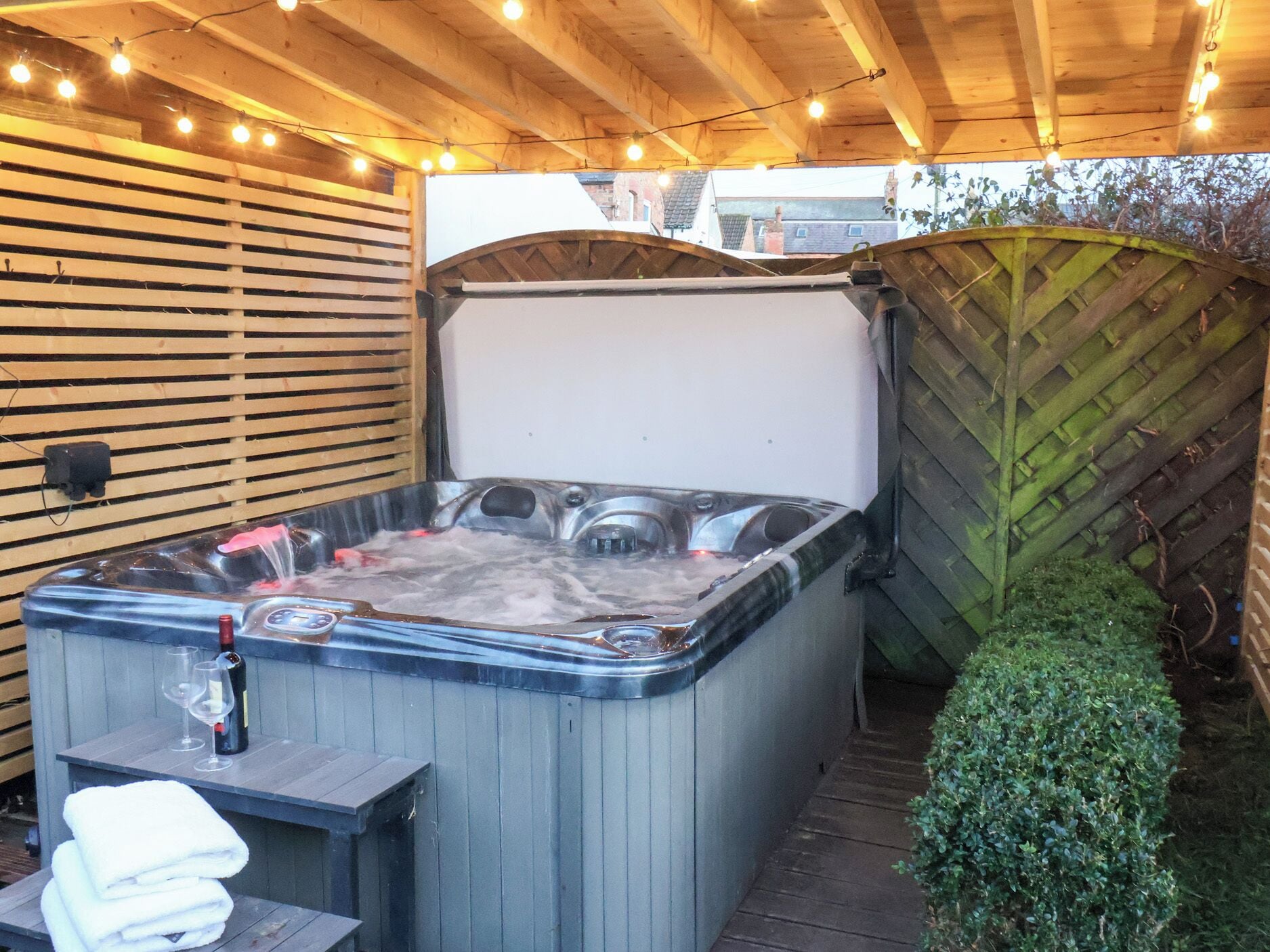 A hot tub with a control panel, a bottle of champagne, and glasses on a wooden table.