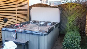 A hot tub with a control panel, a bottle of champagne, and glasses on a wooden table. - Crescent Bay House (Filey)
