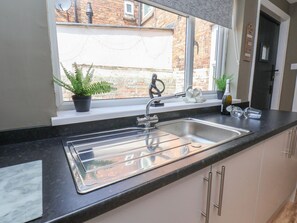 Een keuken met een roestvrijstalen spoelbak, een raam met uitzicht op een bakstenen gebouw, en een plant in een pot op de vensterbank.