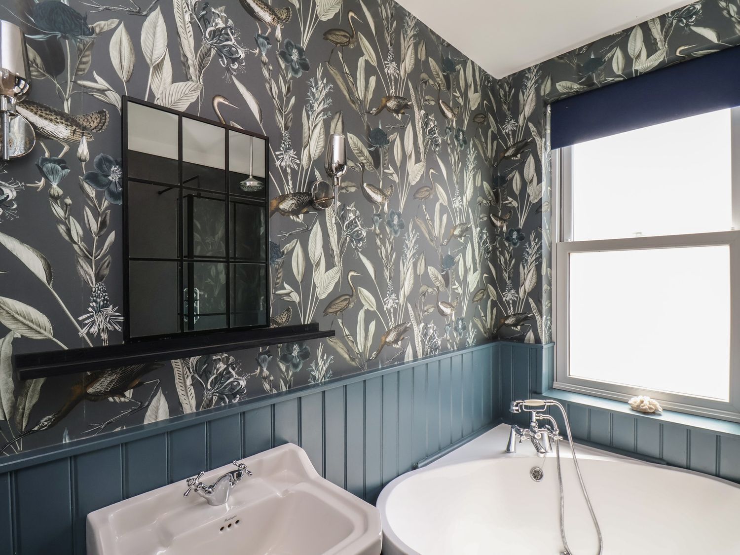 Un baño con papel tapiz floral, un espejo, un lavamanos y una bañera.