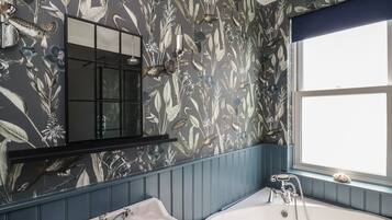 Un baño con papel tapiz floral, un espejo, un lavamanos y una bañera.