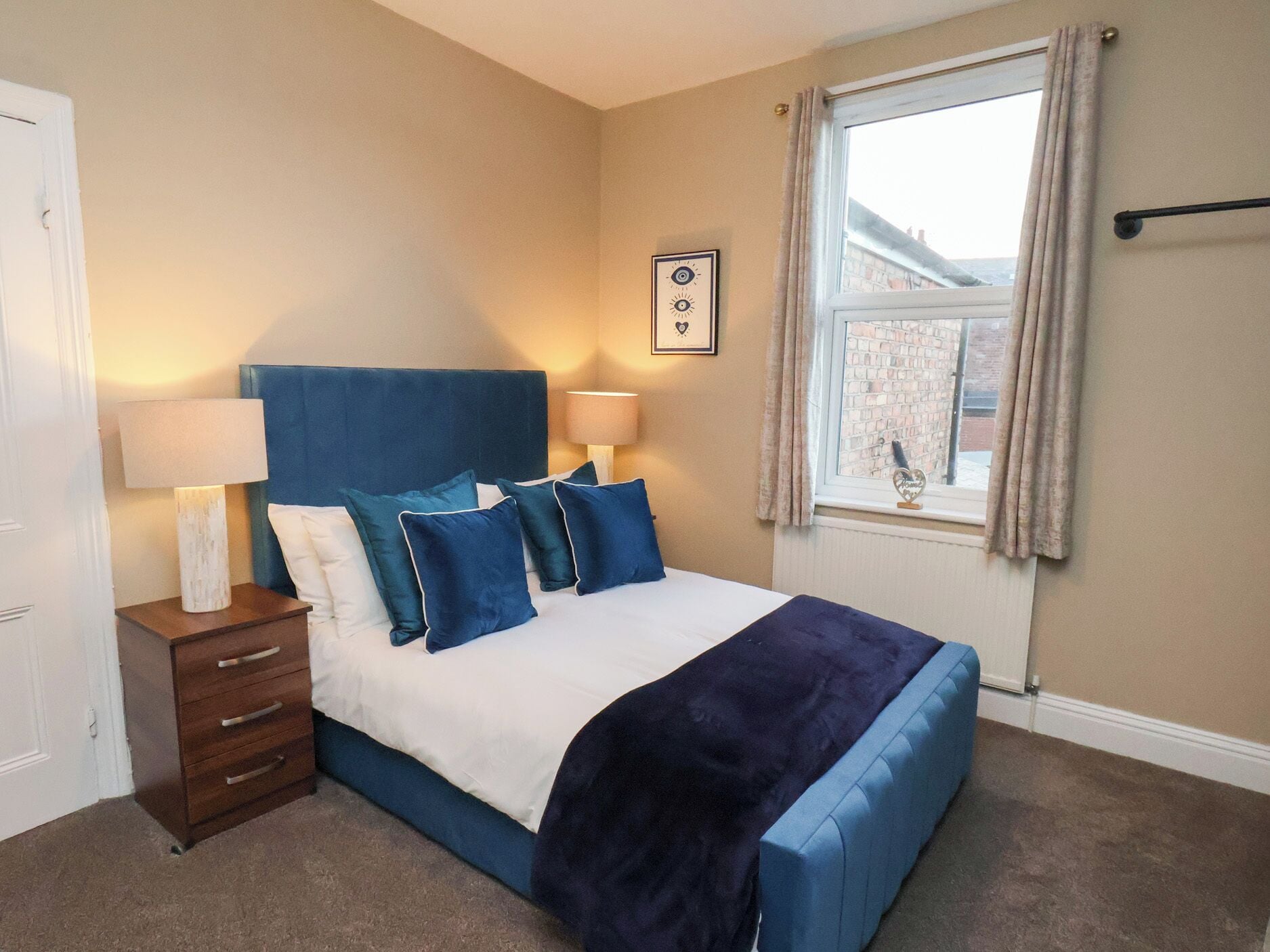 A bedroom with a bed, bedside tables, a window, and a wall-mounted picture.