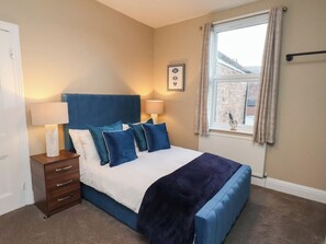 A bedroom with a bed, bedside tables, a window, and a wall-mounted picture. - Crescent Bay House (Filey)