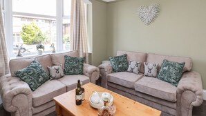 A living room with two beige sofas, patterned cushions, a wooden coffee table with bottles, and a decorative wall piece. - Crescent Bay House (Filey)