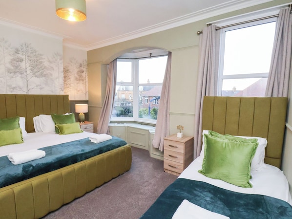 A hotel room with two beds, a window with curtains, a nightstand, and a lamp.