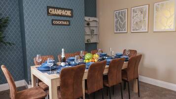 Ein Essbereich mit einer blau gemusterten Wand, einem Schild mit der Aufschrift 'CHAMPAGNE COCKTAILS' und drei gerahmten Pflanzenbildern.