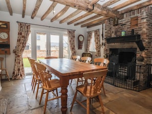 Une salle à manger rustique avec une table et des chaises en bois, une cheminée en pierre et une vue sur l’extérieur.