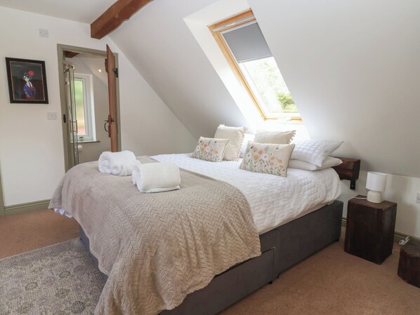 A bedroom with a bed, pillows, a bedside table, a lamp, a window, and a door. - Redwoods (Beverley)