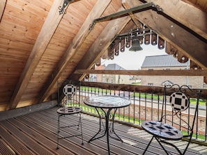 Ein Dachzimmer mit schräger Decke, einem Balkon mit Geländer und Blick auf ein Backsteingebäude.