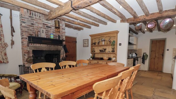 Une salle à manger rustique avec une grande table et des chaises en bois, une cheminée en briques et un buffet en bois agrémenté d’objets décoratifs.