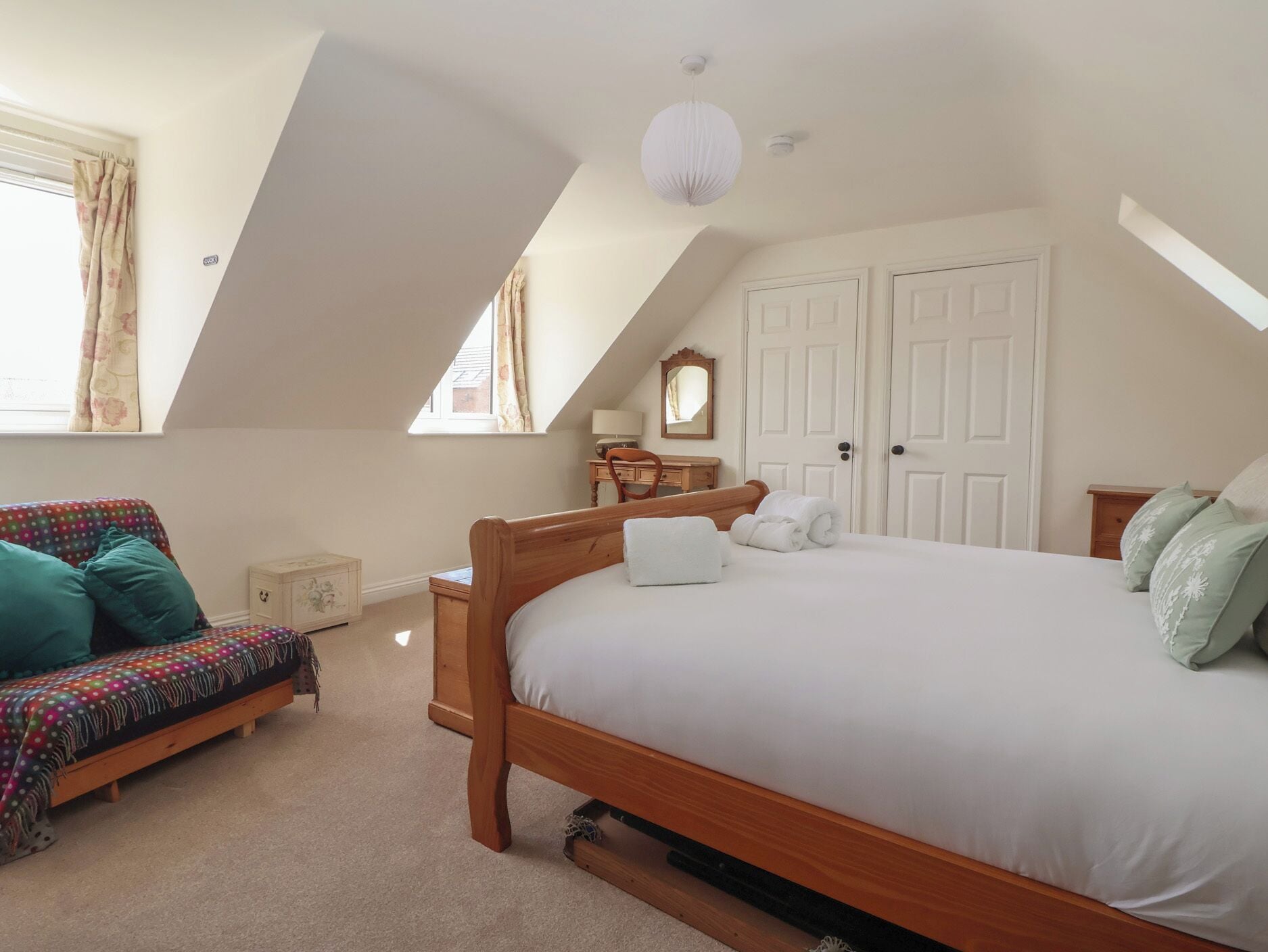 A bedroom with a sloped ceiling, a bed, a chair, a dresser, and a window with curtains.