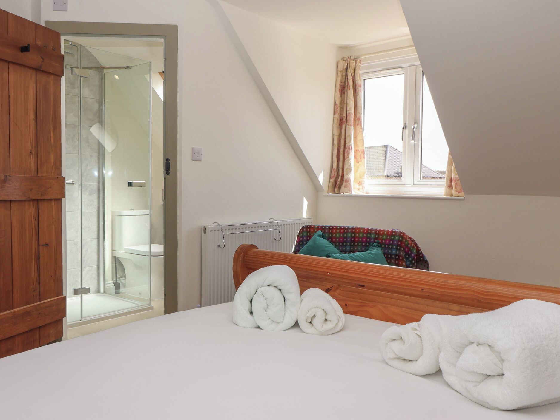 Une chambre avec un lit en bois, une fenêtre avec des rideaux, un radiateur et un espace douche.