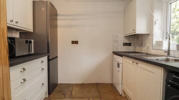 A compact kitchen with white cabinets, a stainless steel refrigerator, a microwave, a dishwasher, and a window with a view.