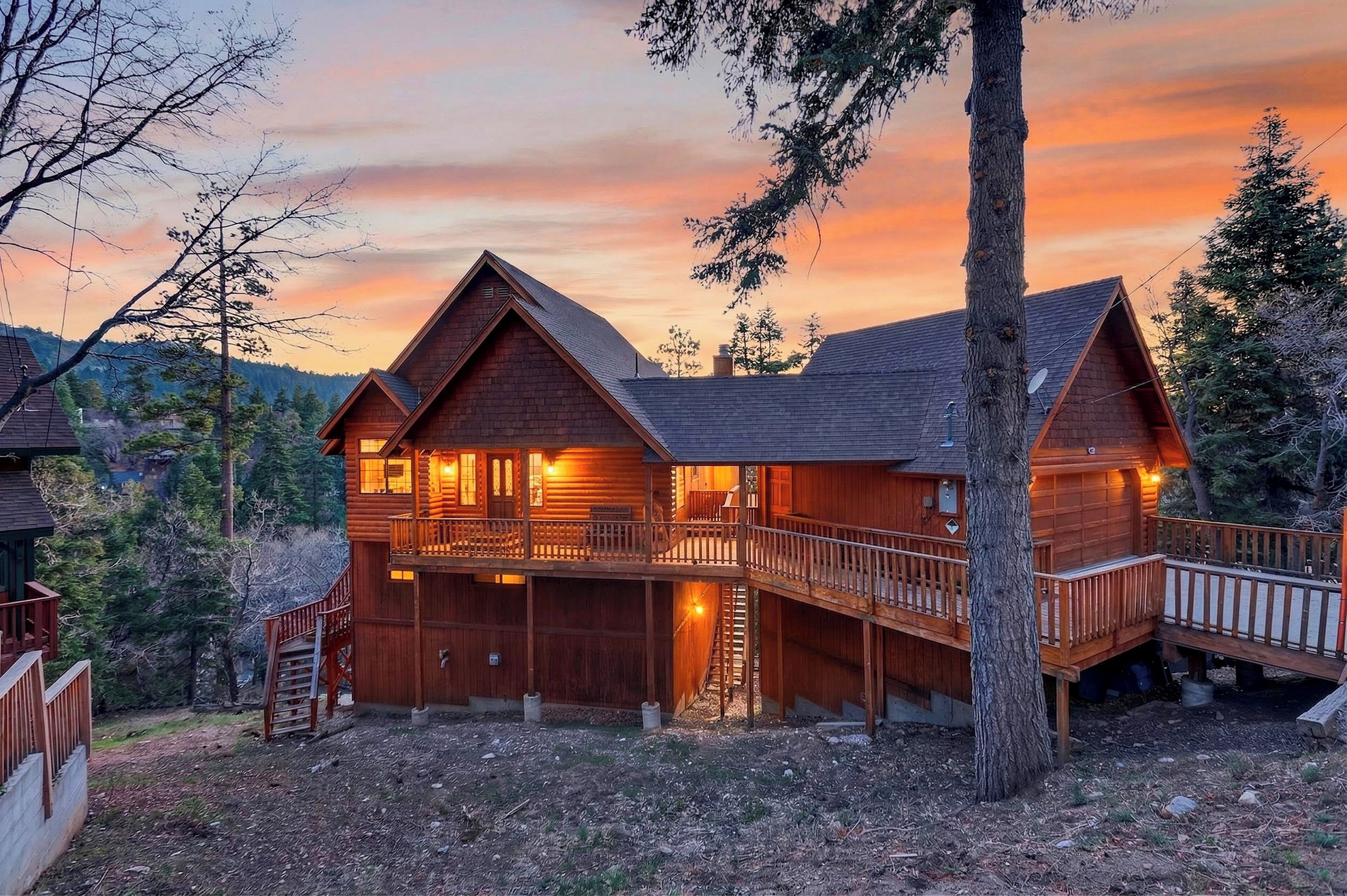 A wooden cabin with a balcony, a staircase, and a view of the surrounding forest.