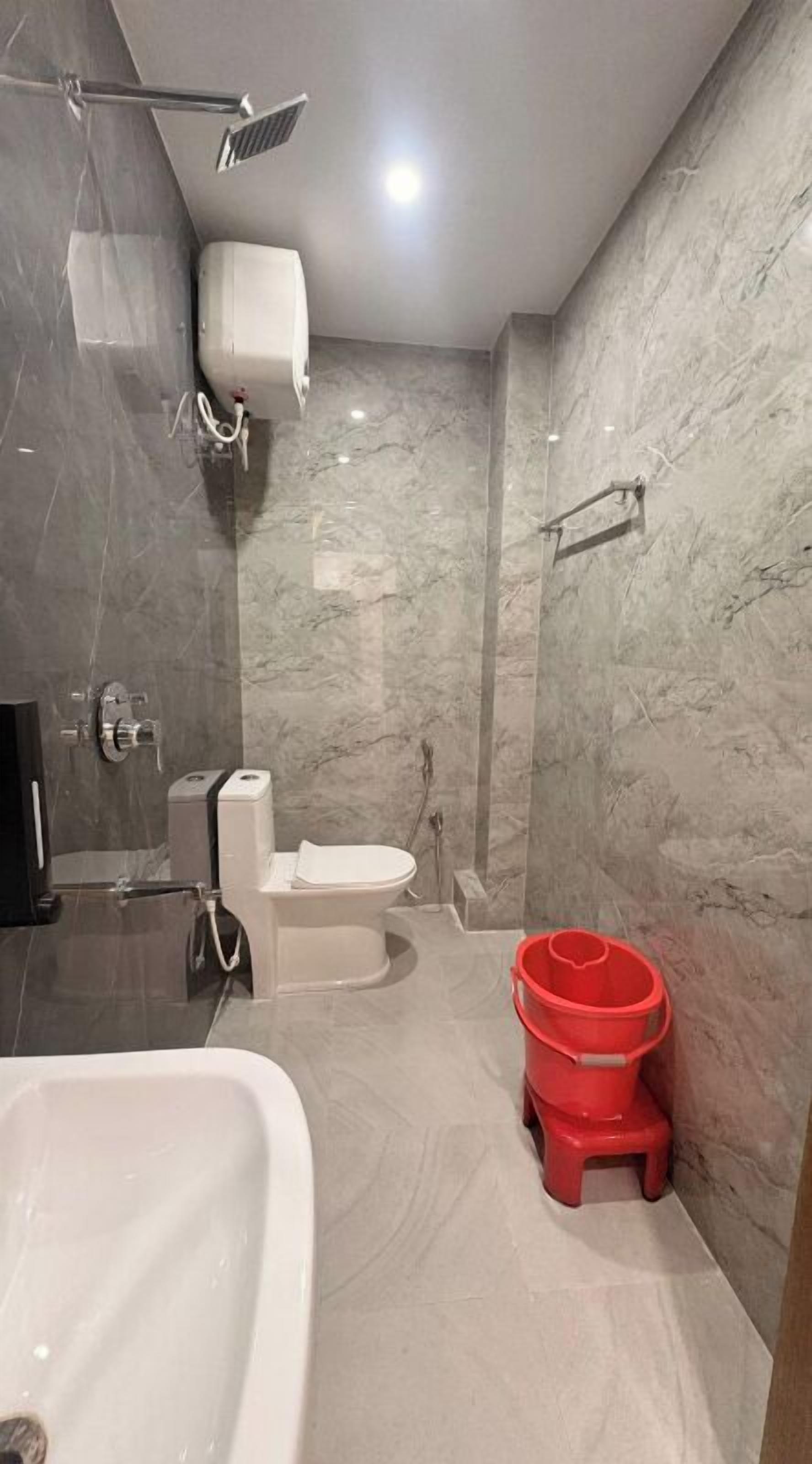 Une salle de bain avec une baignoire, des toilettes, une douche et un seau rouge.