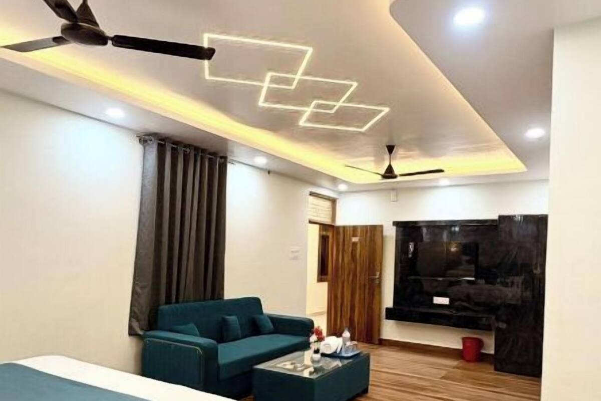 A modern hotel room with a bed, a sofa, a TV, and a ceiling fan.