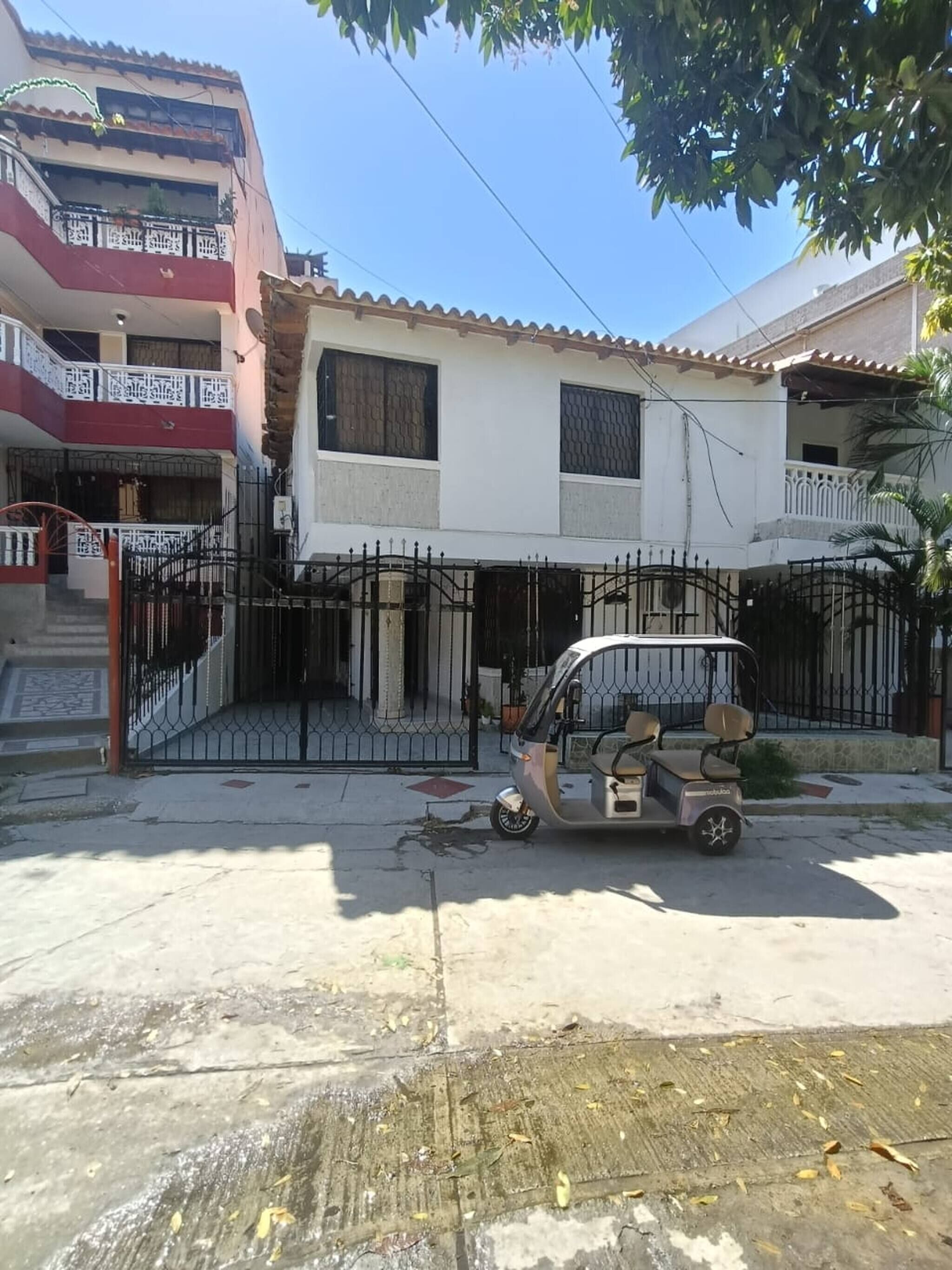 A two-story house with a gated entrance and a parked three-wheeled vehicle.