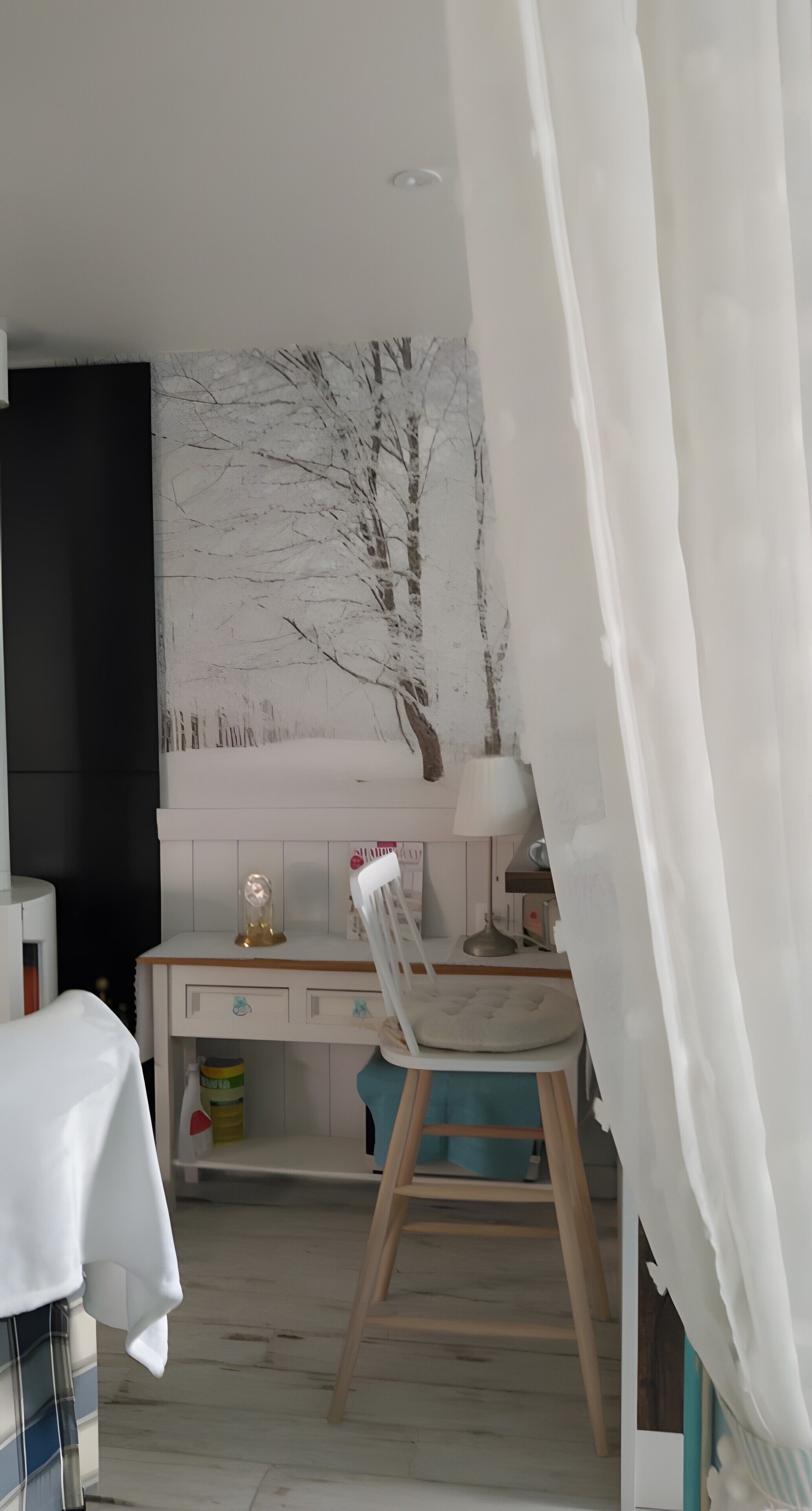 A room with a desk, chair, lamp, and a wall with a tree mural.