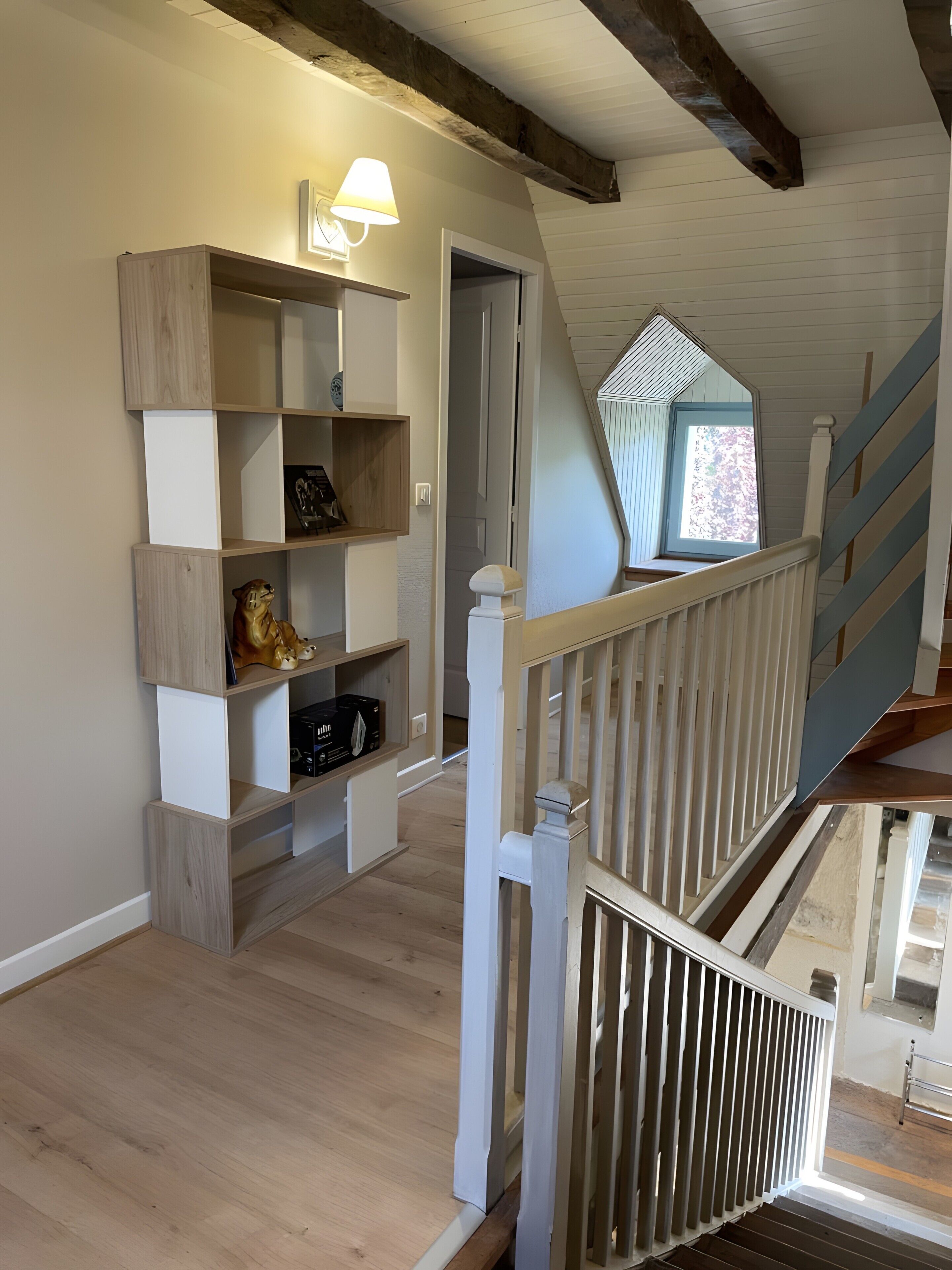 A wooden staircase with a white railing, a built-in shelf unit with decorative items, and a window with a view of trees.