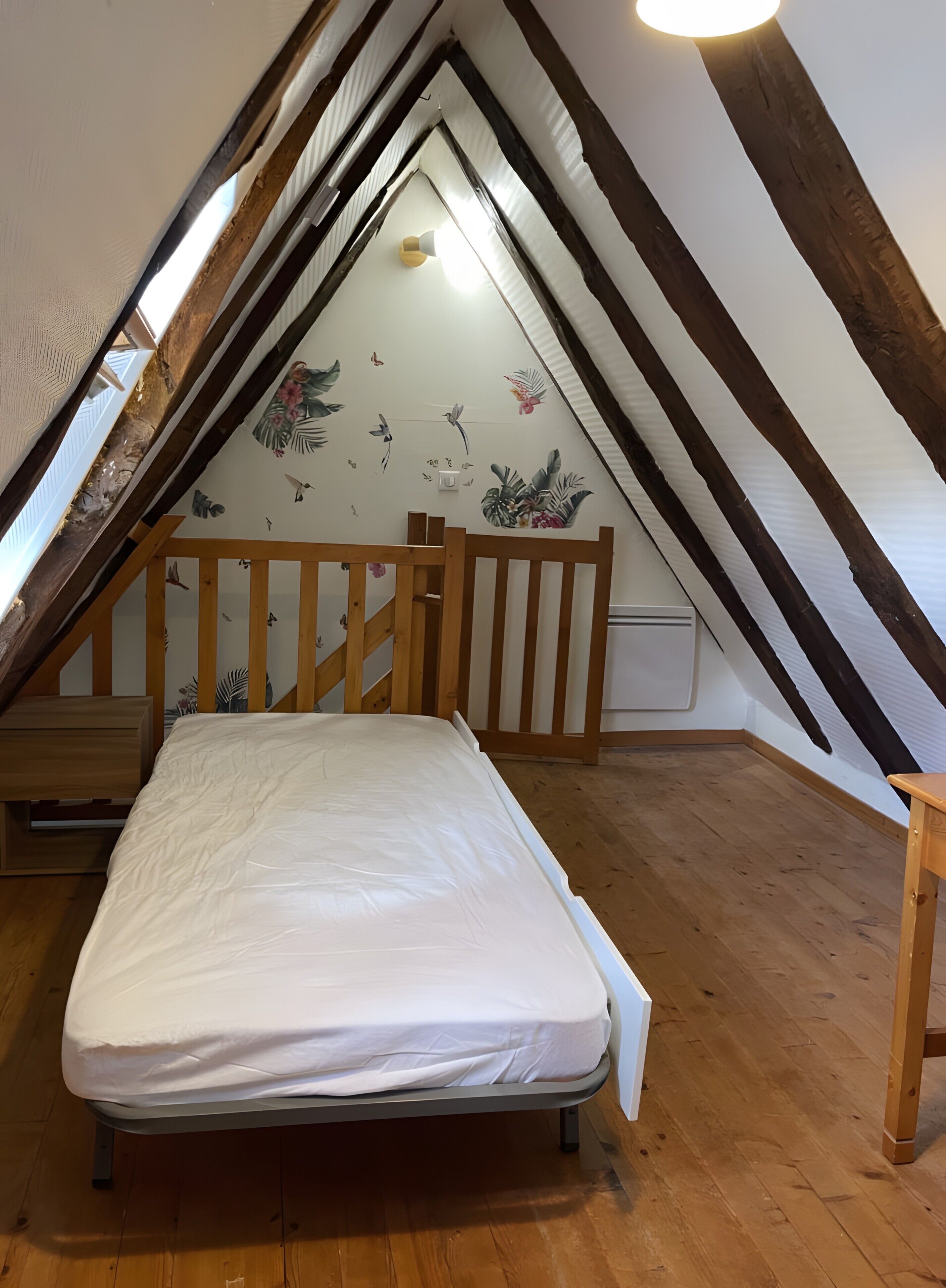 Una habitación pequeña con techo inclinado, una cama individual, suelo de madera y un adorno mural con motivos naturales.