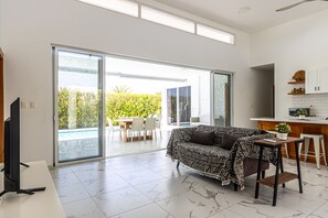 A spacious living area with a sofa, a TV, a dining table, and a kitchen area with a counter and cabinets. - Family Villa with Private Pool in Sosua Ocean Village (Sosúa)
