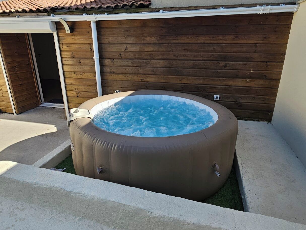 Un jacuzzi dans un jardin, avec une clôture en bois et une porte de garage.