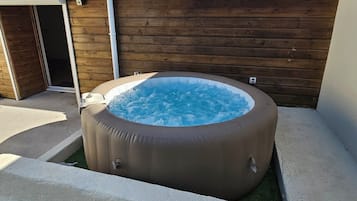 Un jacuzzi dans un jardin, avec une clôture en bois et une porte de garage.