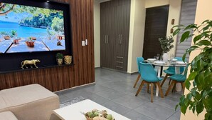 Un salon moderne comprenant un téléviseur, un canapé, une table basse et un coin repas avec des chaises.