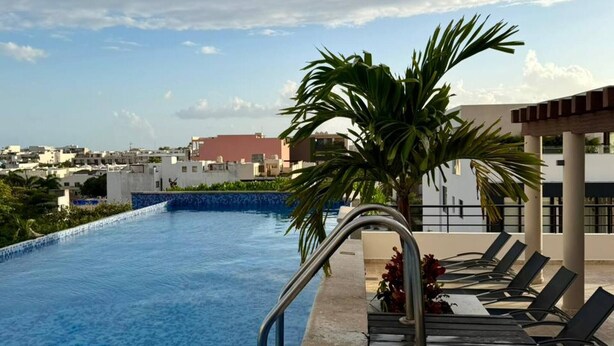 Une piscine sur le toit offrant une vue dégagée sur le paysage urbain, avec un palmier et des chaises longues.
