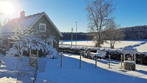 Een huis met een met sneeuw bedekte kap, een omheinde tuin en een bank.