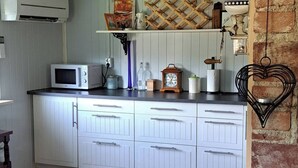 Een keuken met witte kastjes, een magnetron, een spoelbak en een houten plank met decoratieve objecten.