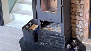 Een houtkachel met schoorsteen, een stenen onderstel en een klein houten kistje met houtblokken.