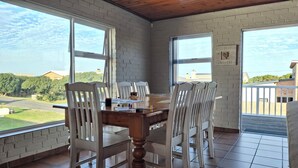 A dining area with a wooden table and chairs, large windows, and a view of a residential area.