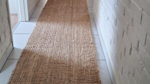 A hallway with a woven rug, white brick walls, and a door leading to another room.