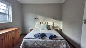 A bedroom with a bed, two nightstands, a wooden cabinet, a window, and a brick-patterned wall.
