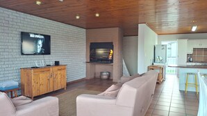 A living room with a brick wall, a television, a wooden cabinet, a sofa, and a kitchen area with a stove.