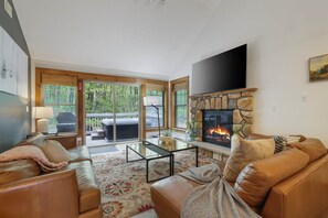 Ein Wohnzimmer mit Kamin, Ledersofas, einem Couchtisch und einem an der Wand befestigten Fernseher.
